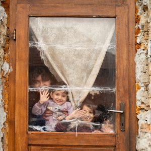 Mamma och barn vinkar genom fönstret till ett hus i behov av stor renovering.