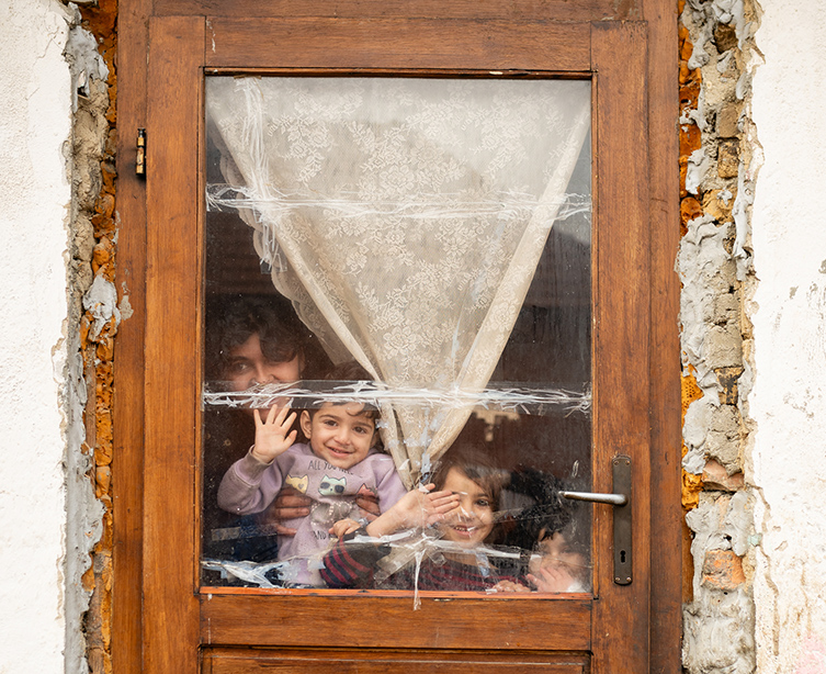 Mamma och barn vinkar genom fönstret till ett hus i behov av stor renovering.