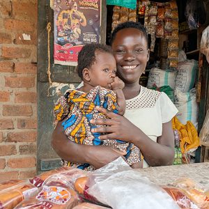Kvinna med litet barn i famnen står i en kiosk.