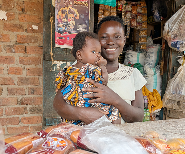 Kvinna med litet barn i famnen står i en kiosk.
