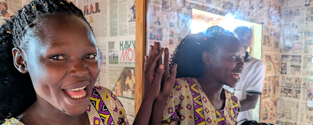 Glad kvinna i Uganda står vid spegel i hårsalong.