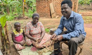Mamma, pappa och en dotter sitter utanför sitt hus i Uganda och rensar bönor.